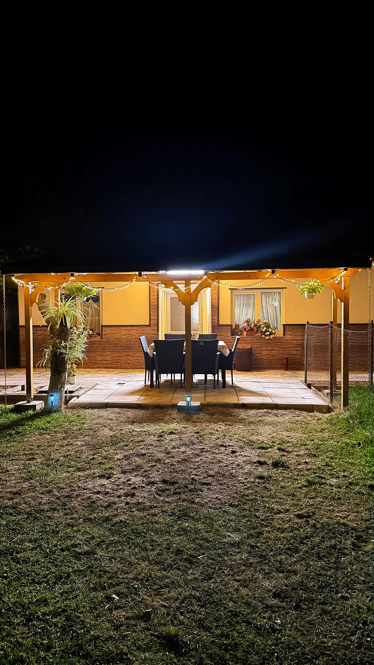 Terasa cu pergolă luminată seara, cu masa pregătită
